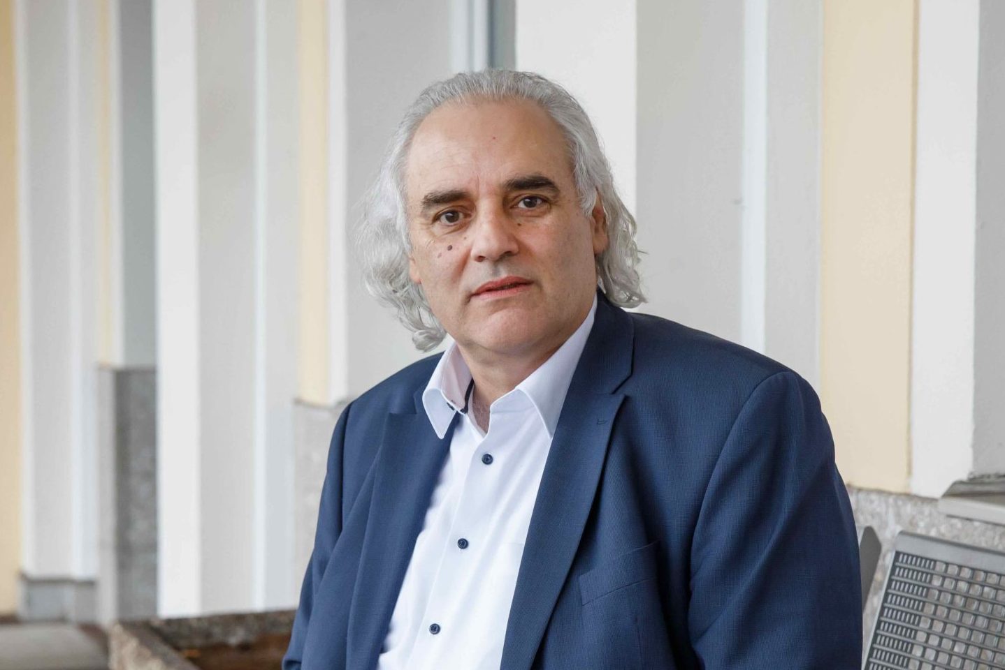 Portrait of Peter Glatz seated on a bench in a university corridor, looking toward the camera.