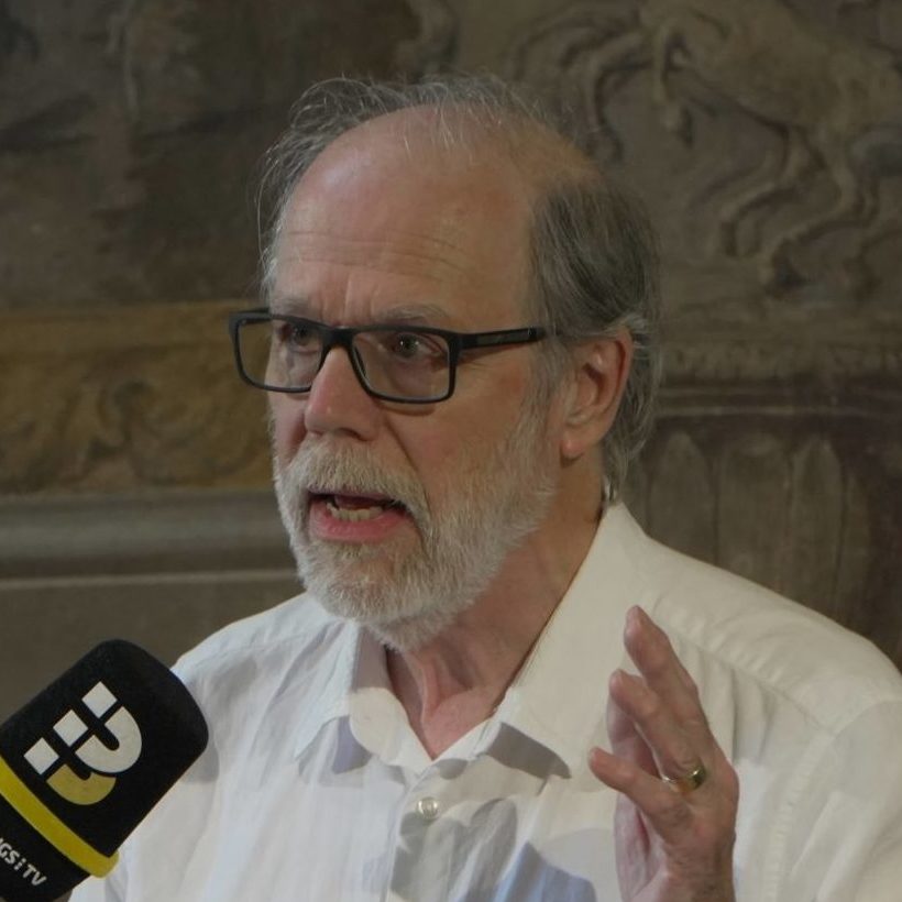 John Bulwer speaking into a handheld microphone during a panel discussion in a historic interior.